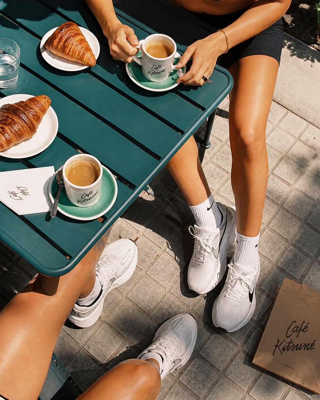 Overhead shot of café table with espresso and croissants beside white sneakers